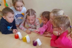 5 dziewczynek i chłopiec obserwują co się dzieje z papierowymi ręcznikami zanurzonymi w kolorowej wodzie.