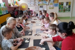 Dzieci siedzą wspólnie z rodzicami przy stolikach, przygotowują pierniki z masy solnej.