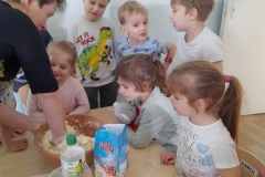 Wychowawczyni przygotowyje masę solna, dzieci siedzą przy stoliku i obserwują.