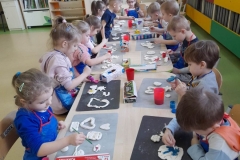Dzieci siedzą przy stolikach, malują farbami pierniki z masy solnej.