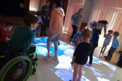 Dzieci bawią się na dywanie magicznym, z boku widać chłopca na wózku inwalidzkim.