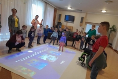 Dzieci stoją wokół magicznego dywanu, jedna dziewczynka łapie rybki.