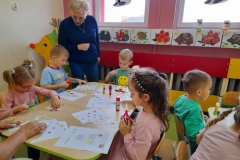 Dzieci siedzą przy stolikach, wyklejają piramidę zdrowia Pani sprawdza czy dobrze wykonują. 