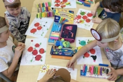 Pięć chłopców I jedna dziewczynka siedzą przy stole, wyklejają jeża, na stole leży kolorowa plastelina oraz piórniki dzieci.