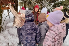 Dziewczynka wsypuje ziarenkami do karmnika, inne dzieci przyglądają się