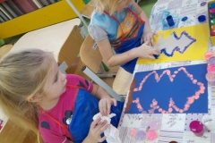 Dzieci siedzą przy stolikach  malują farbami szyszki.