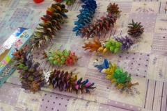 Na stole leżą kolorowe, pomalowane farbami szyszki