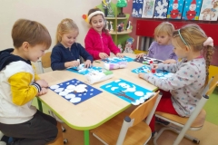 dzieci siedzą przy stoliku i wykonuja obrazki świąteczne za pomocą płatków kosmetycznych.