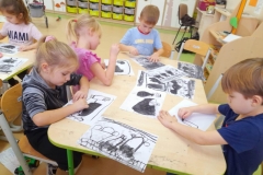 dzieci siedzą przy stoliku i wykonują rysunki weglem drzewnym.