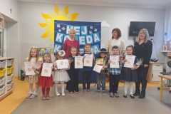 Ośmioro dzieci stoi w półkolu, za nimi trzy panie.