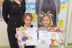 Dwie dziewczynki stoją z dyplomami i nagrodami w rękach, za nimi panie z jury.