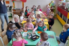 Przy stoliku siedzą dzieci, malują domki z patyczków kolorowymi farbami.