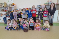 Dzieci ustawione w dwóch rzędach, pierwszy rząd siedzi, drugi stoi. Każde dziecko trzyma w ręku kolorowy domek. W drugim rzędzie obok dzieci stoi Pani, która prowadziła warsztaty.