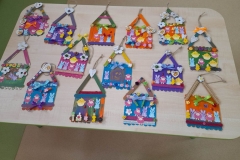 Na stoliku leżą kolorowe domki wykonane z patyczków  pomalowane farbami i ozdobione. Są kolorowe.
