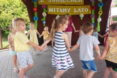 Grupa dzieci w kolorowych strojach trzyma się za ręce tworząc koło.