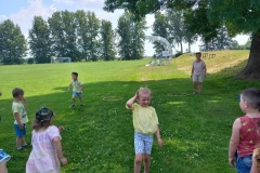 Zdjęcie wykonane na boisku trawiastym. Przedstawia dzieci w biegu.