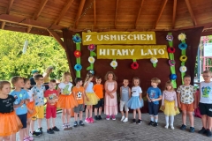 Grupa dzieci w kolorowych strojach stoją w półkolu.