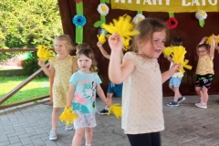 Trzy dziewczynki stoją trzymając w rękach kwiaty.