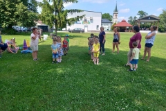 Dzieci stoją w dwóch rzędach. Obok nich kilka osób dorosłych. zdjęcie wykonane w plenerze.