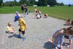 Dzieci ubrane w kolorowe stroje malują kolorową kredą na kostce brukowej.