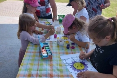 pięć dziewczynek maluje farbami kwiaty. Obok nich stoją dwie panie.