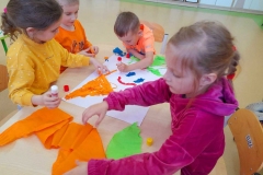 Dwie dziewczynki I dwóch chłopców wyklejają marchewkę z bibuły.
