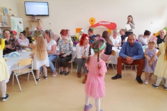 Dzieci podchodzą do rodziców, którzy siedzą przy stolikach, wręczają im kwiaty.