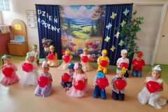 Dzieci siedzą na podłodze, na głowach maja opaski z majowych kwiatów w ręku trzymają czerwone balony.