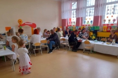Przy stolikach siedzą rodzice, zaproszeni gości oraz kilkoro dzieci.