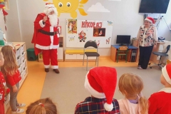 Mikołaj w czerwonym stroju stoi pośrodku sali.