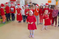 Dzieci ubrane na czerwono stoja w półkolu, dziewczynka w przodzie mówi wiersz