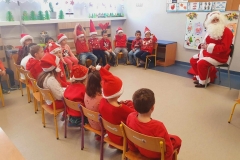 Dzieci siedzą na krzesełkach tworząc półkole. Przed nimi na krześle siedzi Mikołaj.