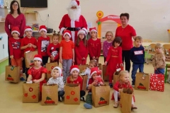 Grupa dzieci stoi z Mikołajem, kilkoro siedzi na podłodze.
