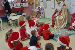 grupa dzieci siedzi przed Mikołajem, z uwaga słucha jego opowieści.