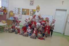 Na zdjęciu widać grupę dzieci ubranych na czerwono w mikolajkowych czapkach. Pośrodku nich stoi św. Mikołaj.