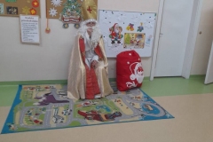 na fotelu siedzi Mikołaj, obok niego stoi worek z prezentami. w tle widać kolorowe gazetki.