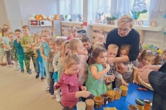 Dzieci stoją  w rzędzie.  Przed nimi stoją  sloiki z miodem.