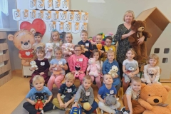 Grupa dzieci siedzi na podłodze. Kilkoro stoi za nimi z tyłu. W tle widnieje napis Dzień Pluszowego Misia. Wysłano Dzieci stoją w dwuszeregu,  każde przytula  do siebie kolorowego misia. Wysłano Dzieci stoją w kole, trzymają misie w rączkach.  W tle żółte  słoneczko namalowane na ścianie. Wysłano Dzieci ubrane w kolorowe  stroje wraz z panią ubraną  na brązowo siedzą  na podłodze.  Przedszkolaki trzymają  w rączkach kolorowe pluszaki. W tle,  sylweta dużego misia i napis. Wysłano Dzieci wraz z panią stoją w kole. W środku na podłodze siedzi  pani ubrana w brązowy strój. Wysłano Wysłano 31 min temu