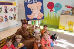 Grupa dzieci siedzi na podłodze, w rękach trzymają różne Misie.