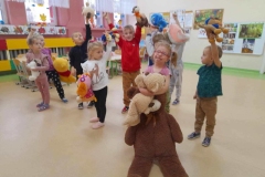 Grupa  dzieci stoi na środku sali. Każde  ma na głowie opaskę  misia. Przytulają do siebie kolorowe pluszaki.