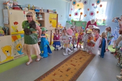 f24583a1-de67-4baf-b7dd-1ac85d9294c5Dzieci ustawione w szeregu tworzą pociąg. Na początku pani w zielonej sukience z worka foliowego z plisowanym dołem z szarego papieru.  Na ramieniu brązowa kokarda. Wśród dzieci pochylona pani w czerwonym swetrze. Na środku podłogi wzorzysty chodnik.