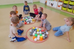 Dzieci siedzą wokół dwóch obręczy, w których są kolorowe piłeczki.