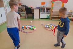 Dwóch chłopców ciągnie kolorowe pileczki w dwóch obręczach.