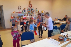 Dziewczynka wraz z wychowawczynią składają na ręce seniorki laurkę oraz prezent.