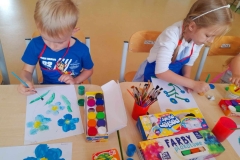 Chłopczyk I dziewczynka malują niebieskie Niezapominajki, na stole widać farby plakatowe.