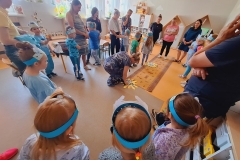 Sala przedszkolna. Dzieci z rodzicami stoją w kole . W środku koła na podłodze 2 słoneczka wyciete z żółtego kartonu ; jedno smutne, drugie wesołe. Na słoneczkach rozłożone obrazki przedstawiające zachowania człowieka wobec przyrody.W środku koła kobieta pochylona dotyka jednego ze słoneczek.