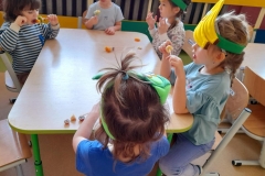 Kilkoro dzieci siedzi przy stoliku, jedzą przygotowane przez siebie szaszłyki owocowe.