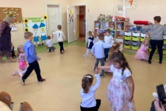 Dzieci tańczą w parach do piosenki, jedno dziecko klęczy, drugie obraca się wokół niego.