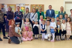 Dzieci ustawione w rzędzie, dwoje z nich siedzi, chłopiec siedzi u mamy na kolanach, druga mama kleczy obejmuje dwie dziewczynki. W tyle stoją rodzice, Dyrekcja ZSP, wychowawczyni oraz wójt gminy.