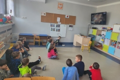 Grupa dzieci siedzi na podłodze i ogładą filmik na telewizorze.